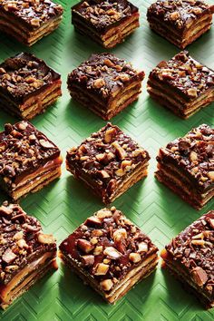 many pieces of dessert sitting on top of a green tray with nuts and chocolate toppings