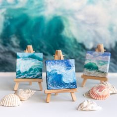 three easels with paintings and seashells on them