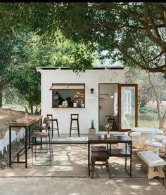 an outdoor dining area with tables and stools under a tree in front of a white building