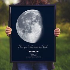 a woman holding up a framed poster with the moon in it's center and words below