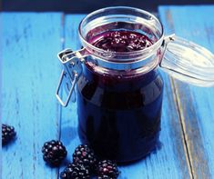 a glass jar filled with blueberry jam on top of a table next to blackberries