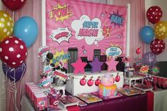 a table topped with lots of decorations and balloons in front of a pink wall mural