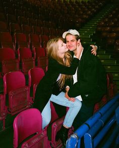 a man and woman kissing in front of an empty stadium seat with pink seats behind them