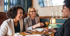 three women sitting at a table laughing together