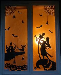 two windows decorated with halloween silhouettes and pumpkins, one is holding a cat