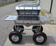 a large metal cart with wheels and grill on the back is parked in front of a building