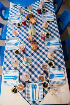 a blue and white checkered table with utensils, plates and cups on it