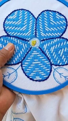 someone is stitching a blue flower on a white cloth