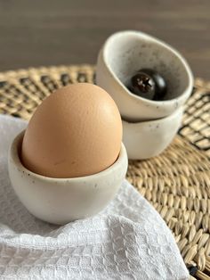 an egg is sitting in a bowl next to another one on a tablecloth with a woven napkin