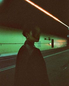 a man standing on the side of a road next to a green light at night