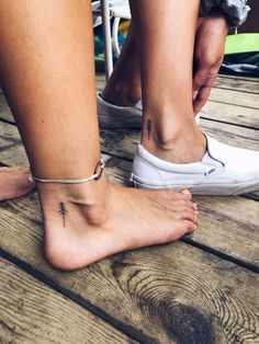 two people with tattoos on their feet sitting on a wooden floor next to each other