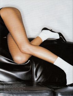 a woman sitting on top of a black leather chair with her legs crossed and wearing white socks