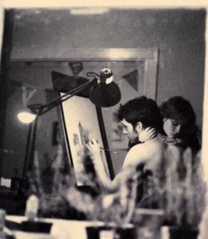 black and white photograph of two people looking at something on a easel in front of a mirror