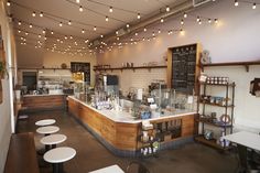 the inside of a restaurant with tables and stools, lights strung from the ceiling