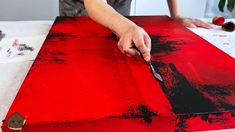 a person is using a knife to paint red and black