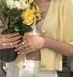 a woman in white pants holding a bouquet of flowers and wearing a yellow cardigan