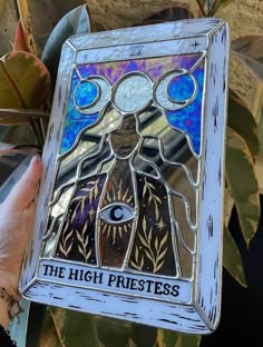 a hand holding up a stained glass window with the words, the high priest on it