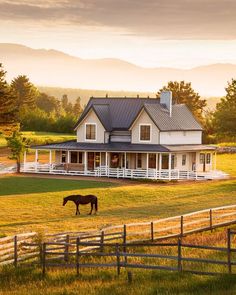 a horse grazes in front of a large white house on a farm with mountains in the background