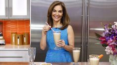 a woman in a blue dress is holding a drink and looking at the camera while smiling