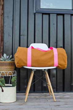 a brown and pink duffel bag sitting on top of a white chair next to a potted plant