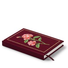 a red book with flowers embroidered on the front and sides, sitting on a white surface