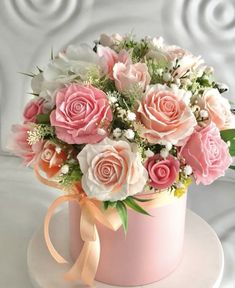 pink and white flowers are in a box on a table with a ribbon around it