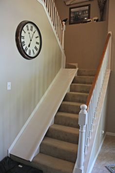 a clock mounted on the wall next to a stair case in a house with carpeted stairs