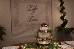 a wedding cake sitting on top of a table covered in greenery and lights next to a christmas tree