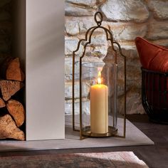 a lit candle sitting in a glass container next to a pile of firewood on the floor