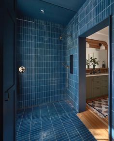 a bathroom with blue tile walls and flooring next to a shower stall in the middle of the room