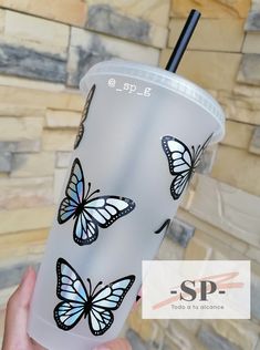 a hand holding a cup with butterflies painted on it and a straw in its mouth