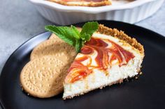 a piece of cheesecake on a black plate with a cracker and mint garnish