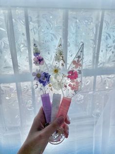 a hand holding some flowers in front of a window