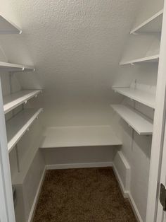 an empty walk - in closet with white shelves and carpeted flooring is shown