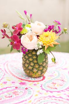 a pineapple vase filled with flowers on top of a pink and yellow table cloth