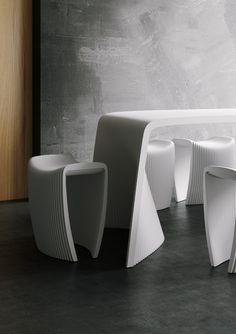 three white tables and two stools in front of a gray wall with concrete flooring