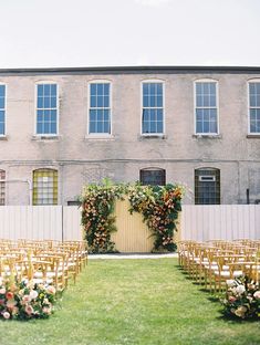 an outdoor ceremony set up with gold chairs and floral arrangements in front of a brick building