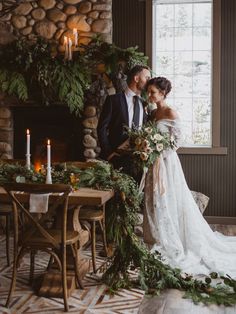 a bride and groom standing in front of a fireplace with greenery on the mantle