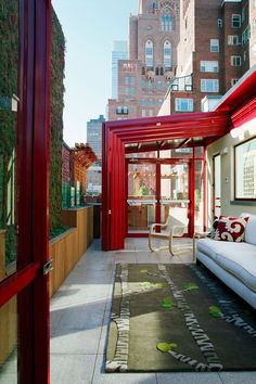 an outdoor living area with red and white furniture on the floor, along with tall buildings in the background