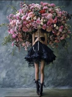 a woman in a black dress holding a large bouquet of flowers over her head with an umbrella