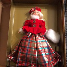 a christmas doll in a cardboard box with plaid dress and fur trimmings on it