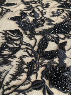 black lace with flowers and beads on it is laying on a tablecloth covered in sequins