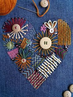 a heart made out of buttons and pins on a blue cloth with yarn in the background