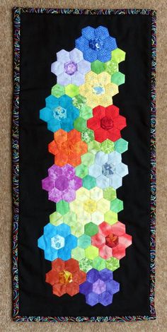 a quilted wall hanging with many different colored flowers on it's black background