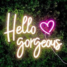 a neon sign that says hello gorgeous with a heart on it in front of some green plants