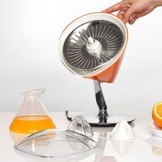 an orange juicer being used as a blender by someone's hand on a white table