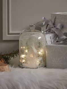 a glass jar filled with lights sitting on top of a white fur covered floor next to presents