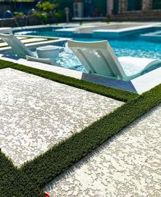 an outdoor swimming pool with artificial grass on the edge and lawn chairs in the background