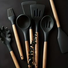 five kitchen utensils are lined up on a black surface with leaves and foliage