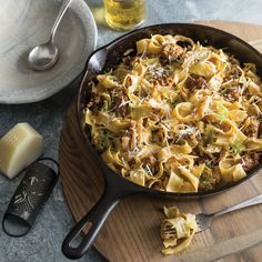 a skillet filled with pasta and meat sitting on top of a wooden cutting board